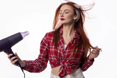 A fashionable woman enjoys drying her hair with a blow dryer, capturing a moment of style and