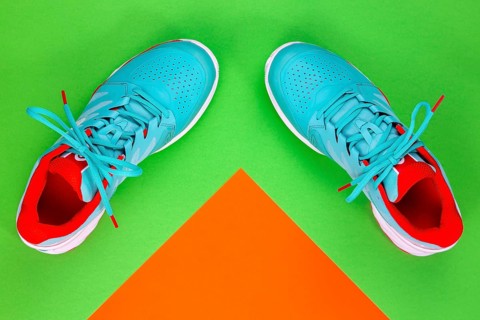 Red, cyan, white pair of new tennis shoes in studio shot over green and orange background. Directly