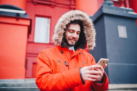 Handsome young male student with toothy smile and beard stands on red wall background, facade of