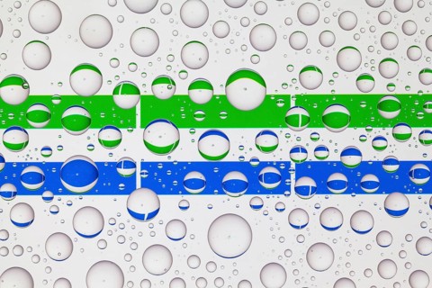 Flags of Sierra Leone behind a glass covered with raindrops. 3D illustration