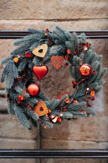 Christmas wreath of fir branches with red Christmas decorations on a stone wall.