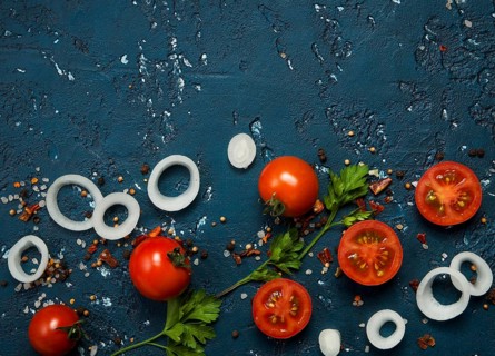 Vegetables background. Fresh vegetables (garlic, tomatoes, onions) on a dark embossed surface. View