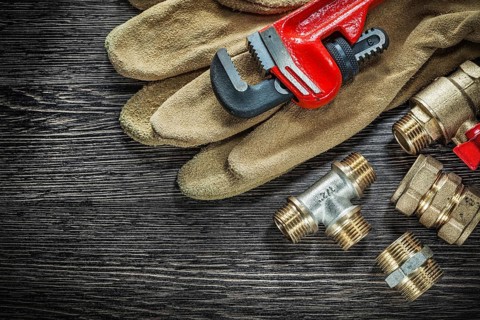 Protective gloves plumbing pipe wrench connectors water valve on wooden board