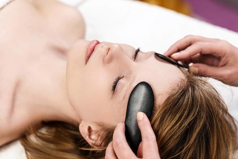 Young woman receiving facial massage with mineral stone