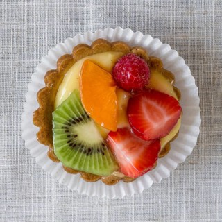 A cake with cream and mixed fruit, resting on linen tablecloth