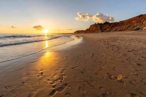 Beautiful sandy beach with red rocks and cliffs. Twilight at sunset with shallow waves on the