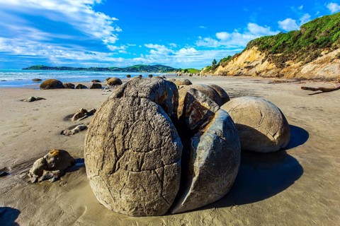 Huge cracked boulder on Moeraki beach. New Zealand. Low tide in the Pacific ocean. The popular