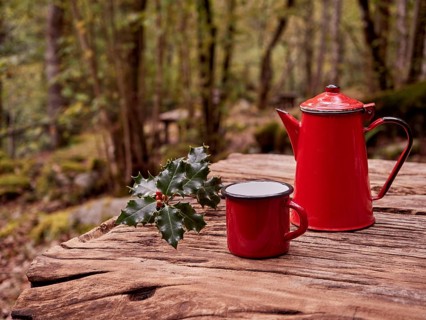 Christmas breakfast in the woods. Sprig of holly next to red mug and vintage coffee pot on wooden