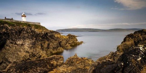 Rocky shoreline with turquoise pools and the historic Broadhaven Lighthouse on a clifftop