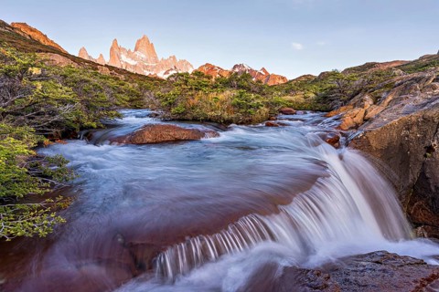A waterfall with the Fitz Roy mountain illuminated by the morning sun in the Los Glaciares National