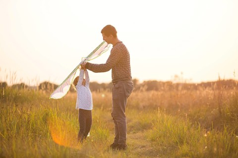 Dad helps his daughter to fly a kite in a field in the summer at sunset. Family entertainment