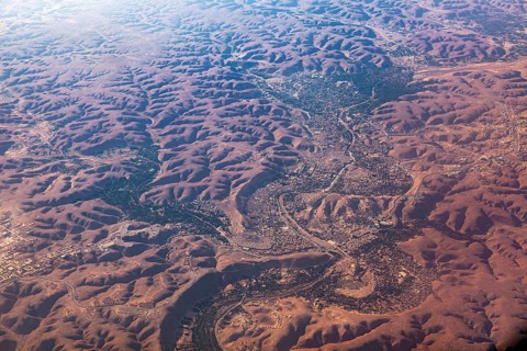 Aerial view of a vast, reddish desert landscape with river valleys and hilly areas, The dunes of