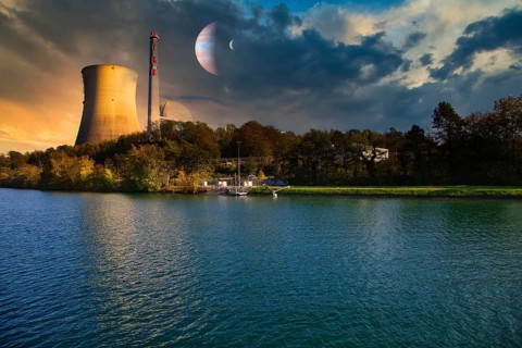 Nuclear power plant with cooling tower on the shore of a body of water at sunset with planets in