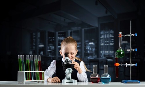 Little girl scientist looking through microscope in classroom at chemistry lesson. School chemical