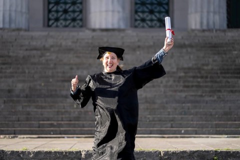 Woman recently graduated, dressed in cap and gown, with her degree in her hand, celebrating