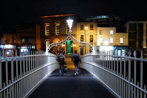 A view of two adults crossing the Ha'penny Bridge on the River Liffey near Temple Bar at night-time