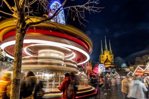 Lebhafte Szene eines Weihnachtsmarktes bei Nacht mit einem Karussell in Bewegung und Kirchtürmen im