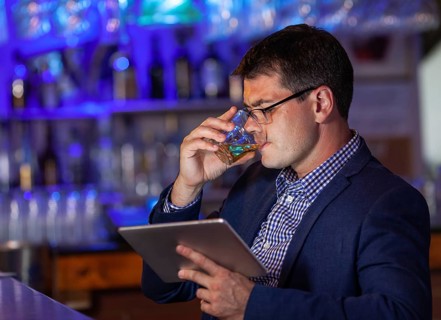 A presentable man in a bar, making a sip from a glass and meanwhile watching at his pad