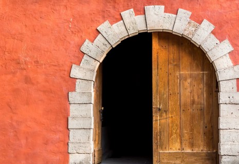Antique arched entrance with double wooden doors, left side opened, and the orange-pink wall