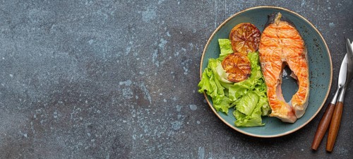 Grilled fish salmon steak and green salad with lemon on ceramic plate on rustic blue stone