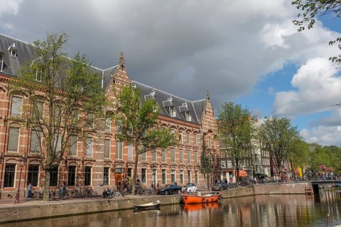 Historic buildings and boats along a canal, trees and cloudy sky, Amsterdam, Netherlands