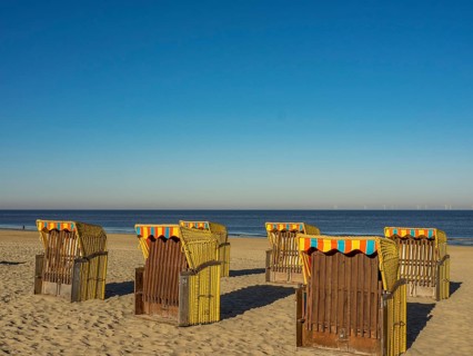Several beach chairs stand on the sandy beach overlooking the calm sea on a clear, sunny day,