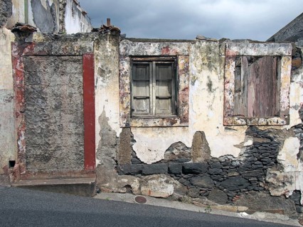 An old ruined house partly collapsed on a sloping street with a blocked up door crumbling walls and