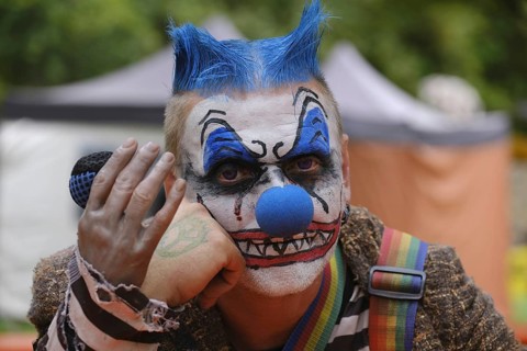 A clown with a microphone and striking make-up, menacing atmosphere outdoors
