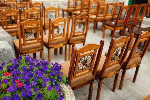 Wooden chairs with patterns on the backs stand in rows on paving stones.