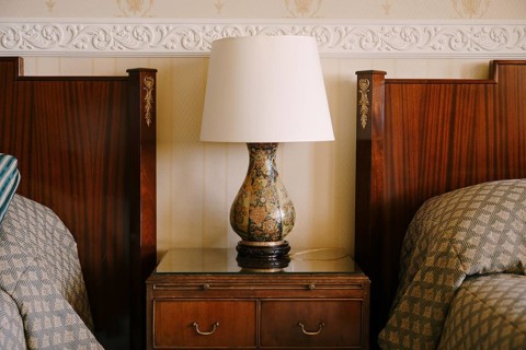 Bedside lamp on the nightstand. Refined and rich interior. Wooden bedside table next to two beds.