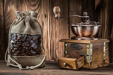 Vintage sack with coffee beans and wooden mill on wood background