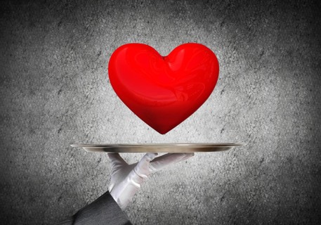 Cropped image of waitress's hand in white glove presenting big red heart on metal tray with dark