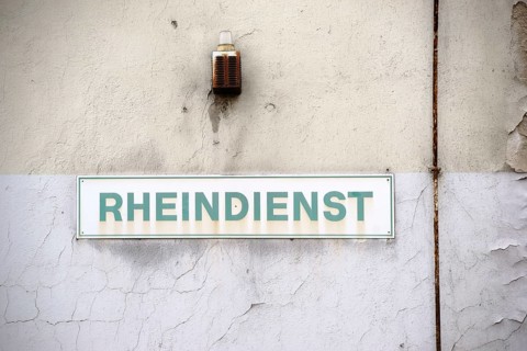 A close-up of a warning light with a rusty siren and a sign on the wall of an industrial ruin