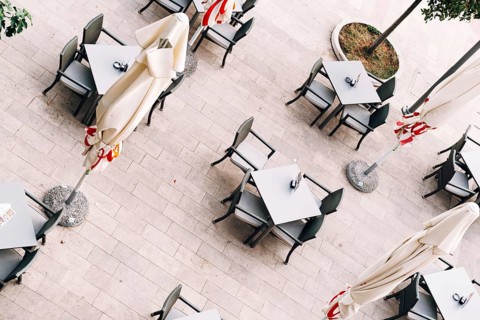 Top view of tables and chairs near folded beach umbrellas on tiles.