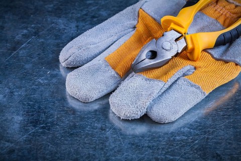Protective gloves with pliers on scratched metallic background construction concept