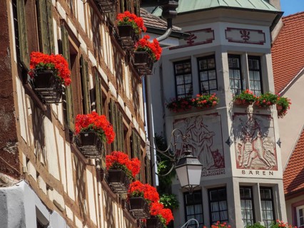 Historic half-timbered house with windows and red flowers under a blue sky, Meersburg, Lake