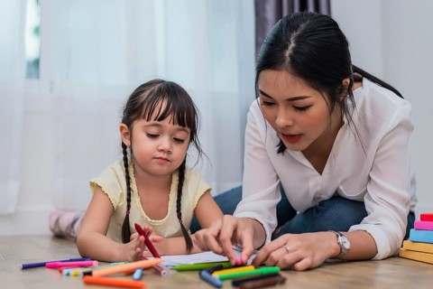 Mother teaching girl in drawing class. Daughter painting with colorful crayon color in home.