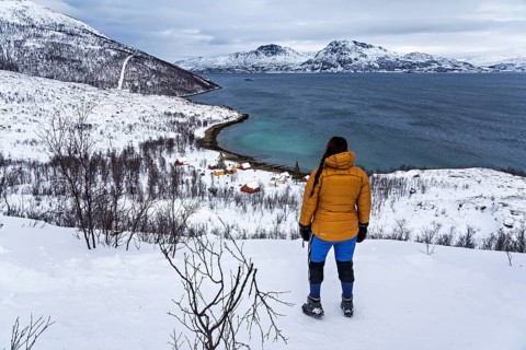 A woman in winter clothing stands above the small bay of Skjellvika on the island of Kvaloya,