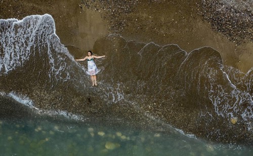 Woman with swimsuit and white dress resting on a sandy beach with breaking waves on the shore.
