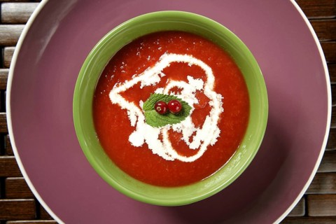 Mediterranean tomato soup with basil and redcurrant in a colorful green dish over wood