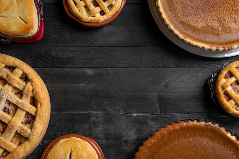 Kitchen table full of different pies, pumpkin pies, apple pies, with empty space in the middle.