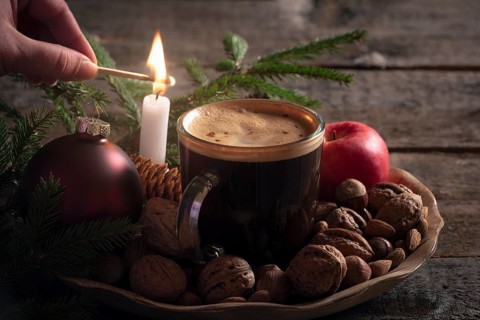 Christmas cozy atmosphere with a woman lighting a candle on a wooden platter full with nuts, apples