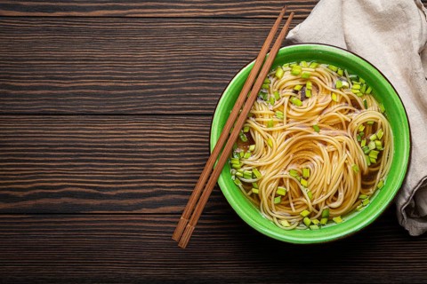 Asian noodles soup in green rustic ceramic bowl with wooden chopsticks top view on dark wooden