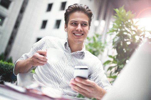 Happy handsome businessman looking at computer screen while typing something on laptop keyboard