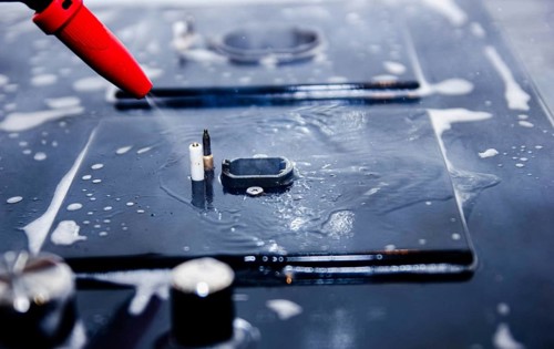 Close-up of a red nozzle spraying water onto a soapy stove surface