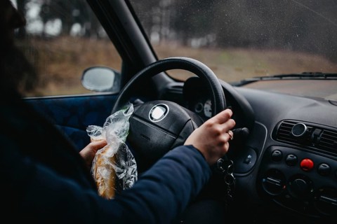 Person holding a sandwich and steering wheel in a car, capturing a casual driving moment