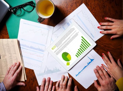 Business team hands at work with financial reports and a tablet computer, top view