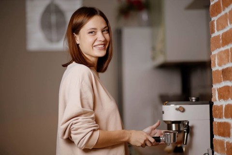 Woman smiling while using an espresso machine next to a brick wall
