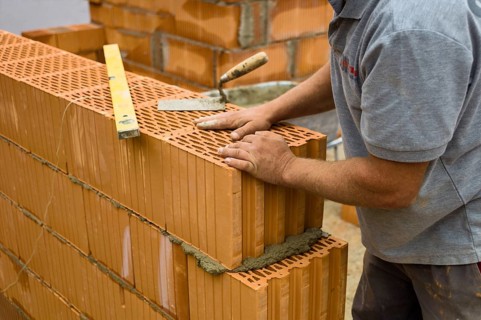 Anonymous construction worker on a building site erecting a brick wall. Brick wall of a solid house