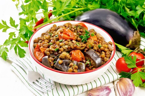 Green lentils stewed with eggplant, tomatoes, garlic and spices in a bowl on a napkin, parsley on